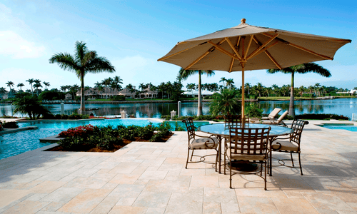 Florida pool house with coral stone tiles in French pattern used as elegant pool deck stone around a luxury waterfront swimming pool